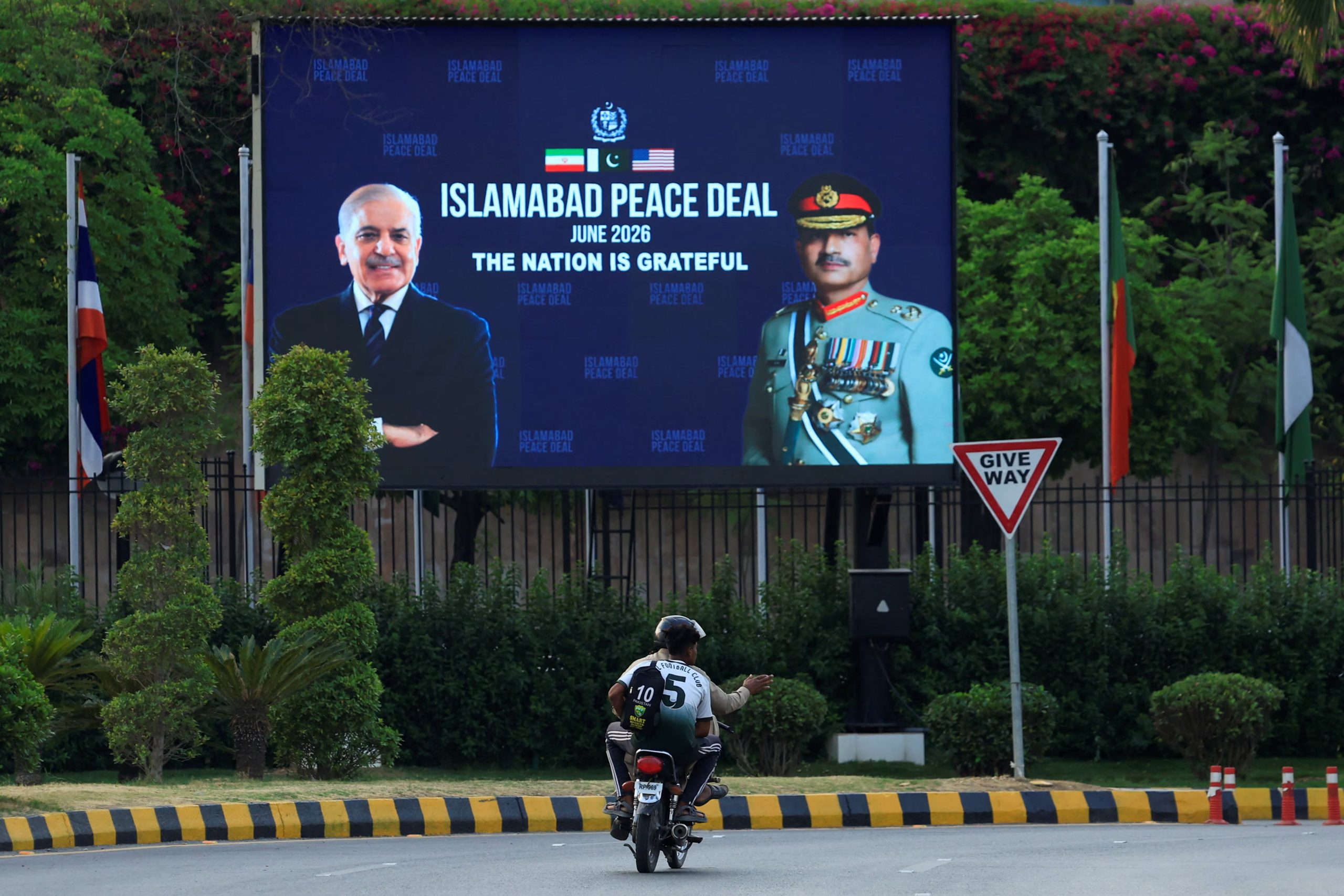 Men ride a motorbike past a roadside billboard displaying portraits of Pakistan's Chief of Army Staff General Asim Munir and Prime Minister Shehbaz Sharif, following a deal between the U.S. and Iran, in Islamabad, Pakistan, June 16, 2026. REUTERS/Akhtar Soomro