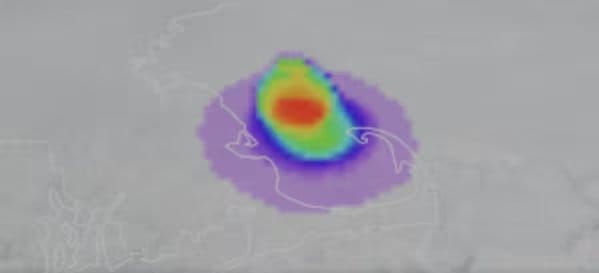 Una vibrante visualización de datos en forma de calor, con tonos que van del púrpura al rojo, se superpone a un mapa borroso de una región costera, destacando un área concentrada. (Captura de video)