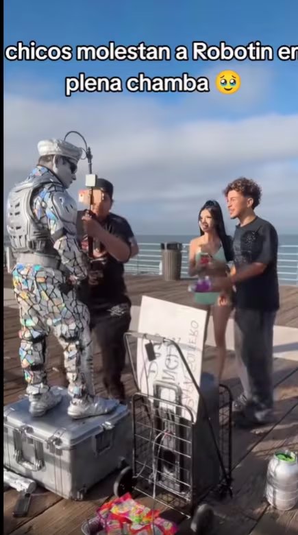 La imagen muestra a Robotín, un artista callejero, siendo grabado por jóvenes mientras realiza su performance en un muelle en Estados Unidos.