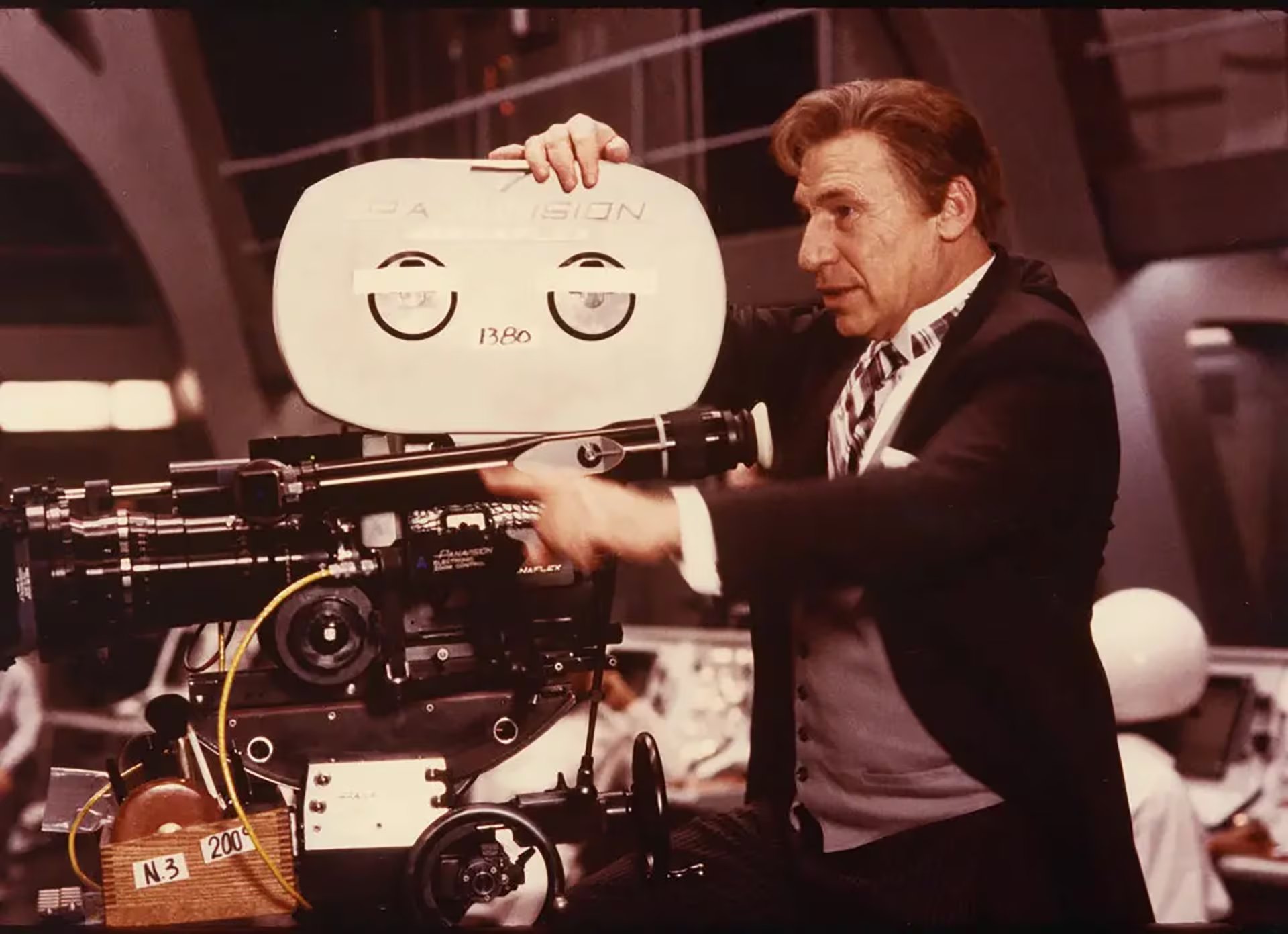 Performance M, una figura clave del conjunto musical, ajusta una cámara de cine profesional Panavision en el set, preparándose para capturar la esencia de una actuación.