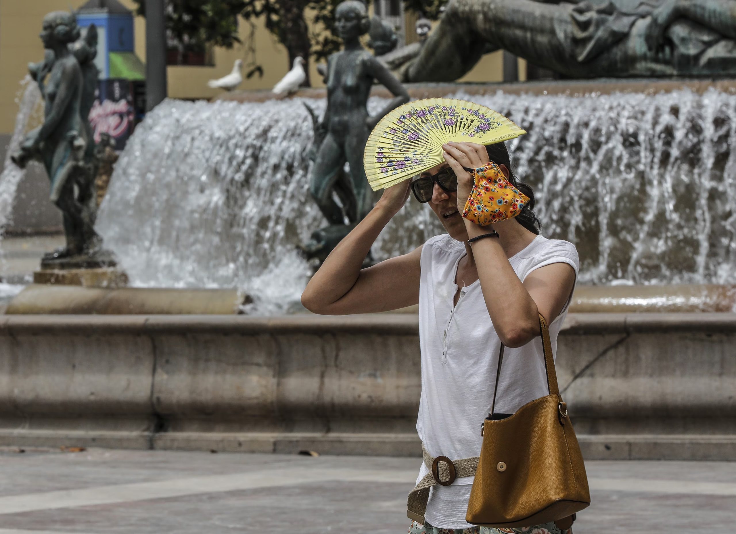 Una mujer se tapa la cabeza con un abanico para guarecerse de las altas temperaturas cerca de una céntrica fuente de a 12 de julio de 2021, en Valencia. (Rober Solsona - Europa Press)