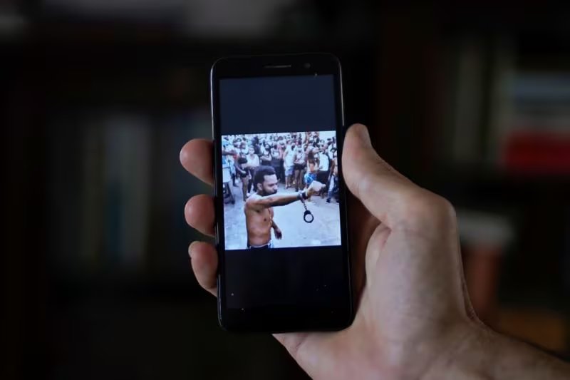 Un hombre muestra en su teléfono móvil una imagen difundida en las redes sociales del rapero Maykel Osorbo con esposas sujetas en una muñeca, en La Habana, Cuba. 6 de abril de 2021 (REUTERS/Alexandre Meneghini/Archivo)