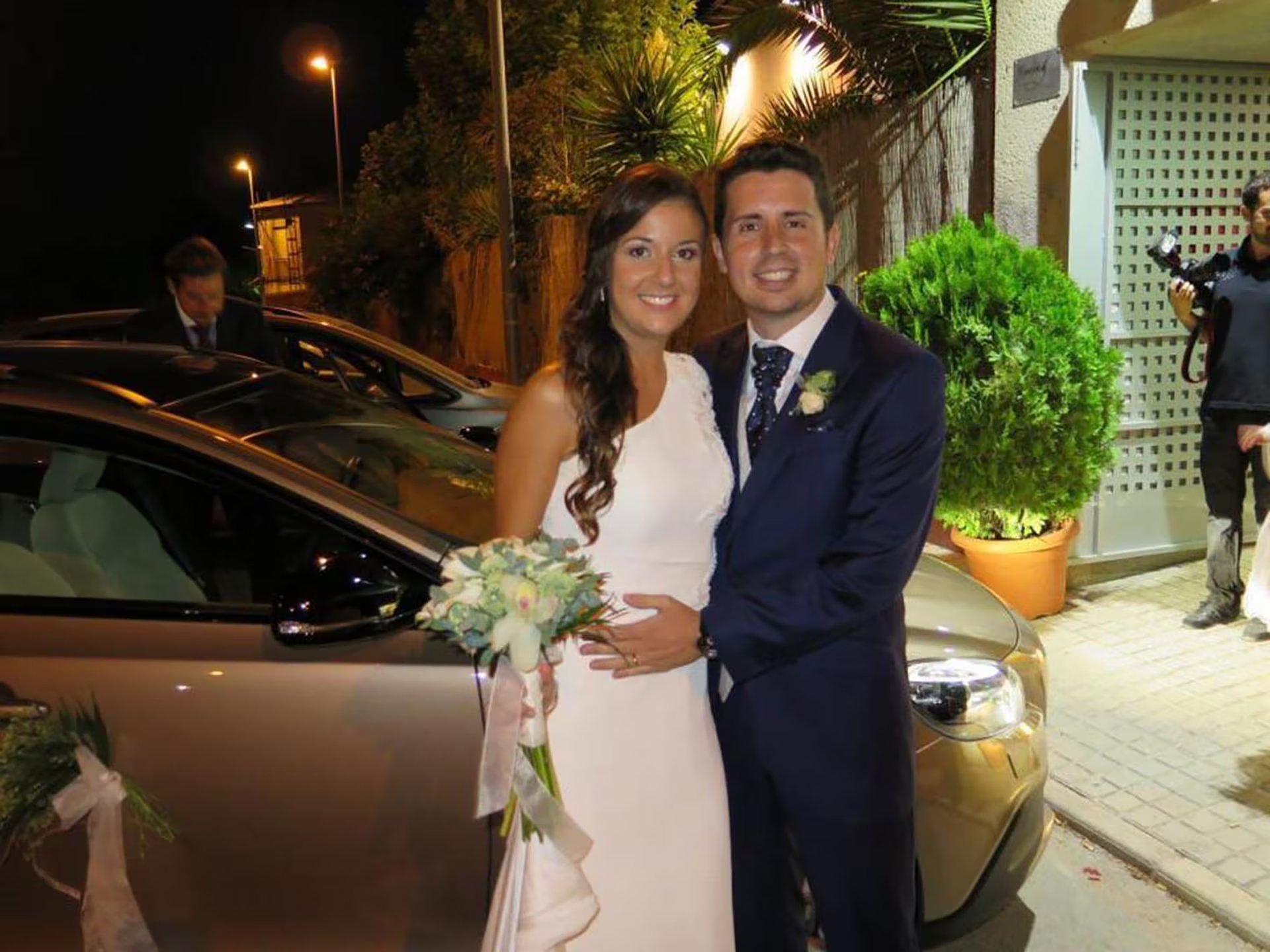 Maje Moreno Cant&oacute; y su pareja, vestidos con traje nupcial, posan sonrientes en el exterior junto a un veh&iacute;culo decorado para la celebraci&oacute;n.