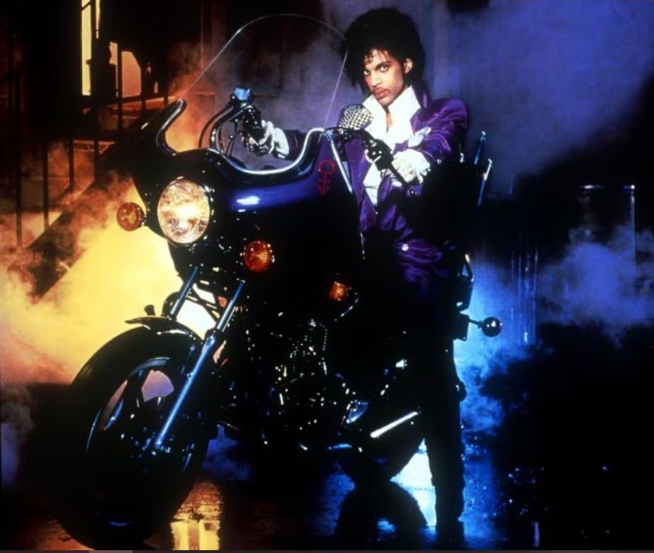 Prince, en su ic&oacute;nico atuendo morado, posa junto a su motocicleta personalizada para la pel&iacute;cula y &aacute;lbum 'Purple Rain'